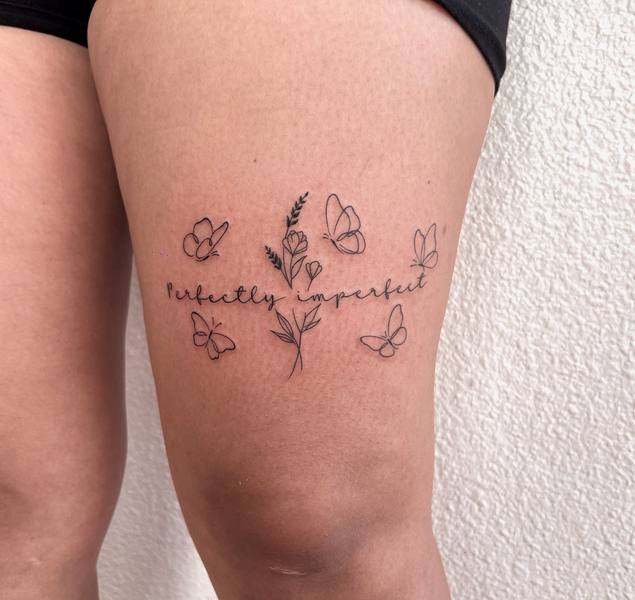 Perfectly Imperfect script with butterflies and florals fine line thigh tattoo by Cihan Pohrenk in Venice, Los Angeles