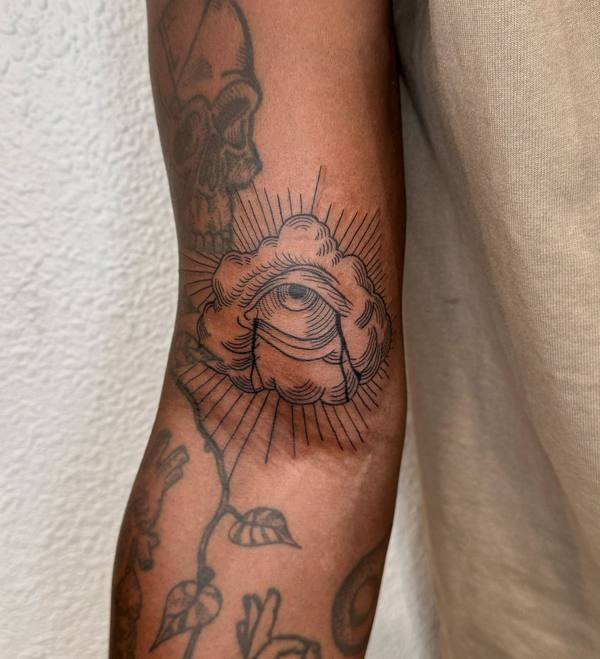 Eye in clouds with rays fine line elbow tattoo by Cihan Pohrenk in Venice, Los Angeles