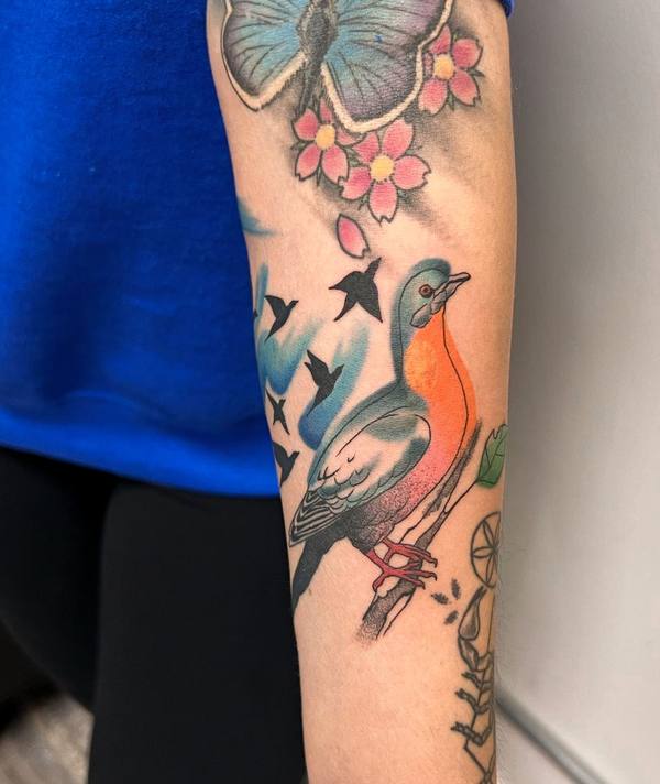 Colorful bird with cherry blossoms and swallows forearm tattoo by Cihan Pohrenk in Venice, Los Angeles